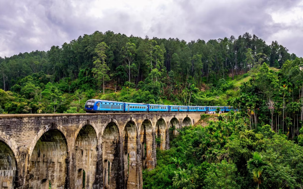 The blue train crossing the historic Nine Arch Bridge in Ella, surrounded by tea estates. Private Sri Lanka Tours, Ceylon diary travels. Best Ella Sri Lanka Guide - Nine Arch Bridge Train